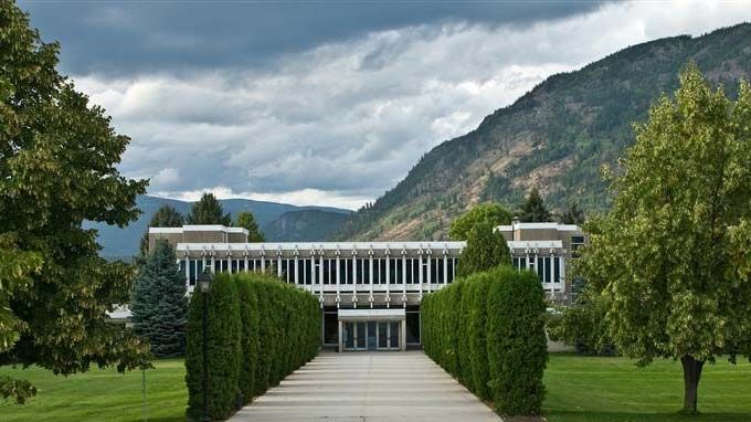 Main campus building with green trees leading up a cement walkway under an overcast sky